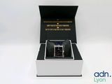une boîte ouverte contenant une montre, posée sur une surface blanche