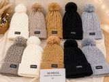 six bonnets tricotés de couleurs différentes, ornés de pompons, posés sur une table