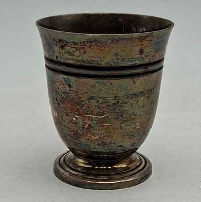 une tasse en métal posée sur un socle en bois, sur une surface blanche