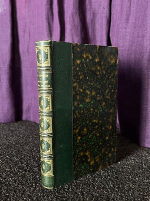 un vieux livre vert posé sur une table, à côté d'un rideau violet