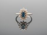 a close up of a blue sapphire and diamond ring on a reflective surface