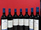six bottles of red wine lined up on a wooden table