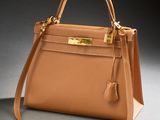 a brown leather handbag with gold hardware on a grey background