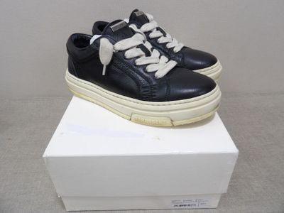 baskets en cuir noir avec des lacets blancs, posées sur une boîte blanche