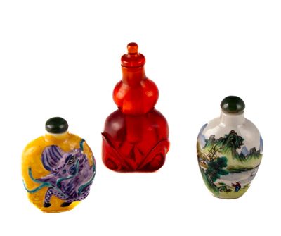 trois bouteilles en verre de couleurs différentes, ornées de motifs, posées sur une surface blanche