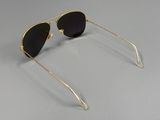 une paire de lunettes de soleil dorées aux verres noirs, posée sur une surface grise
