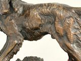 bronze statue of a dog on a rock with a red leash