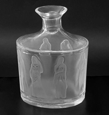 black and white photograph of a clear glass bottle with three figures on it
