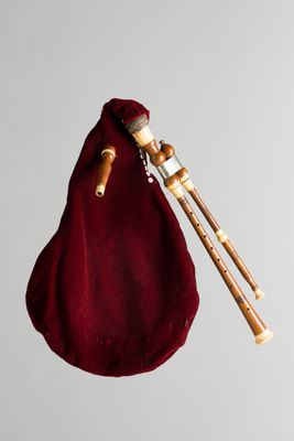 quelqu'un tient un sac contenant une cornemuse et une paire de baguettes en bois