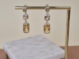 silver and citrine earrings on a gold stand on a pink surface