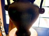 un vase noir posé sur un tabouret en bois devant une fenêtre