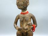 une statue en bois représentant une femme tenant un chat qui porte un collier de perles rouges