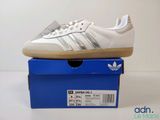 une paire de baskets Adidas blanches posées sur une boîte bleue