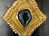 une image représentant une broche bleue et dorée posée sur une surface noire