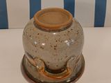 a brown vase sitting on a table with a blue striped chair behind it