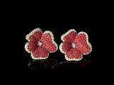 une paire de boucles d'oreilles en forme de fleurs, composées de diamants rouges et blancs, posées sur un fond noir
