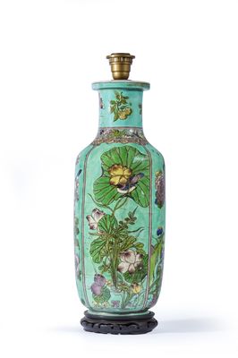 a green vase with flowers on it sitting on a stand