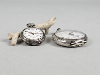 two silver pocket watches sitting next to each other on a table