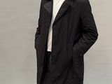 un homme vêtu d'un manteau noir et d'un jean, debout, les mains dans les poches