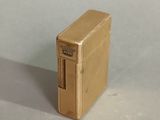 a gold lighter sitting on a table with a white wall behind it