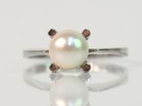 un gros plan d'une bague en perle blanche posée sur une surface blanche