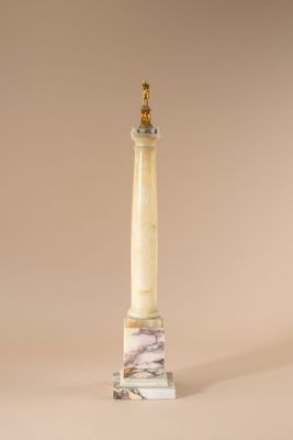 une colonne en marbre blanc surmontée d'un chapiteau doré, sur fond beige