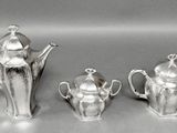 three silver teapots and a coffee pot sitting on a table