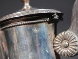 a silver tea pot with a handle on a table