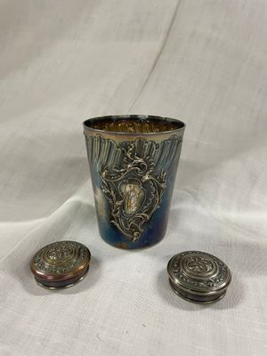 une tasse plaquée argent et deux boutons en argent sur un tissu blanc