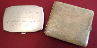 two silver cigarette cases with writing on them sitting on a red surface