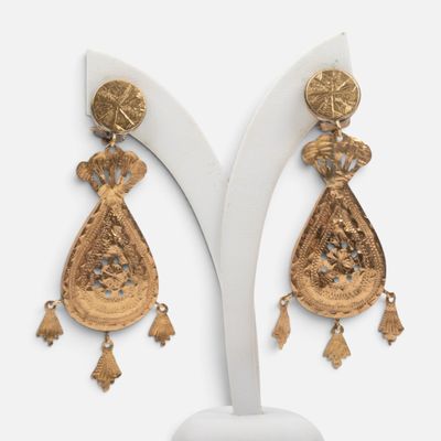 une paire de boucles d'oreilles en or ornées de pompons, posée sur un présentoir blanc