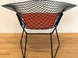 a black wire chair with a red cushion on a wooden floor