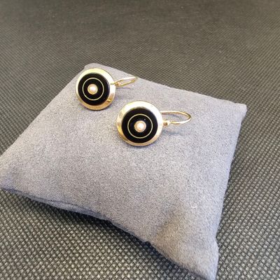 boucles d'oreilles argentées et noires posées sur un coussin, sur une surface grise