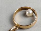 gold plated ring with a pearl pendant on a white surface