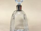 flacon de parfum en verre transparent muni d'un bouchon argenté, posé sur un fond blanc