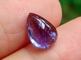 une personne tient une pierre précieuse violette dans la main, sur un fond vert
