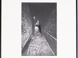 photographie en noir et blanc d'une personne marchant dans une rue étroite