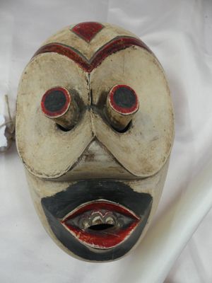 un masque en bois posé sur un drap blanc, avec une brosse à dents