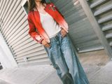 a woman that is standing on the sidewalk with her hands in her pockets