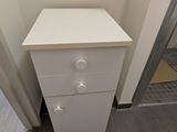 a small white cabinet in the corner of a bathroom