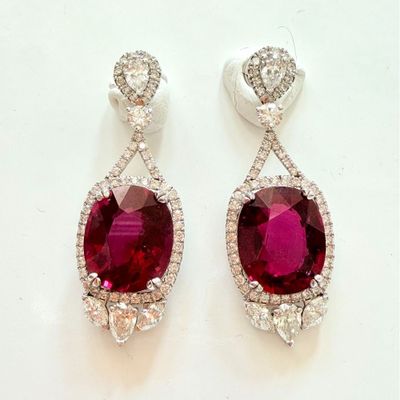 deux paires de boucles d'oreilles en rubis et diamants posées sur un fond blanc