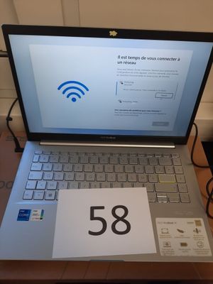 un ordinateur portable posé sur une table, sur laquelle se trouve une pancarte