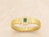 a close up of a gold bracelet with a green stone