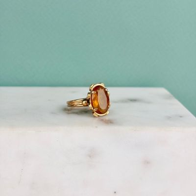 une image représentant une bague en or sertie d'une citrine facettée, posée sur une dalle de marbre