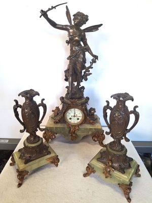 trois statues en bronze posées sur une table sur laquelle se trouve une horloge