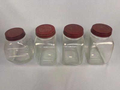 quatre bocaux en verre avec des couvercles rouges sont alignés sur une surface blanche