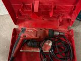 une perceuse électrique dans une boîte à outils rouge, avec son cordon d'alimentation