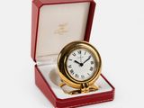 a small gold clock in a red box on a white surface