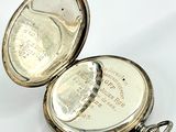a silver pocket watch that is open on a white surface