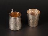 two silver cups with designs on them sitting next to each other